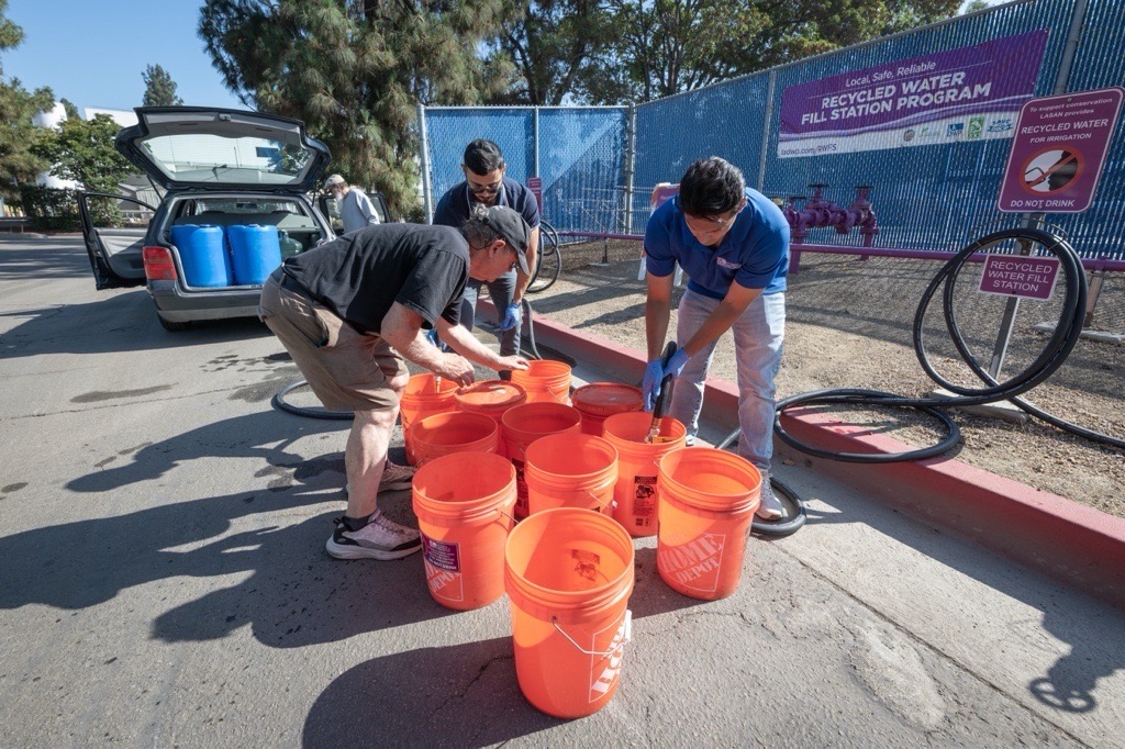 a group of men filling large orange buckets with recycled water for customers