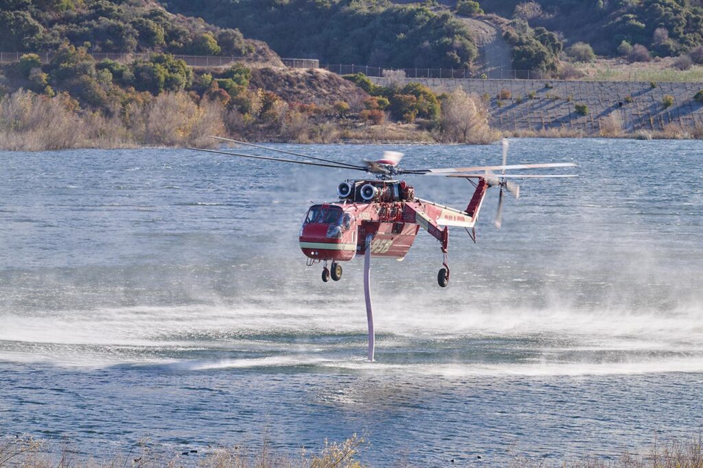 red aerial fighting helicopter getting water from the open air Encino Reservoir to help fight the Palisades wildfire