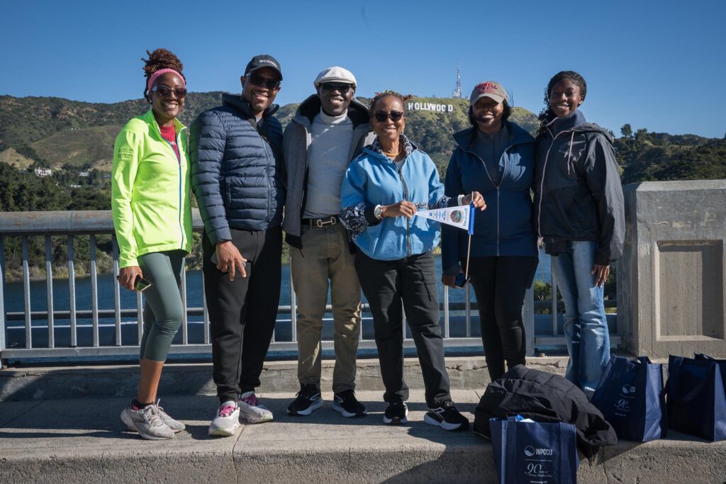Community members pause for a photo atop the historic Mulholland Dam during LADWP's Reservoir Walk at the Hollywood Reservoir. The Hollywood sign is seen in the background.