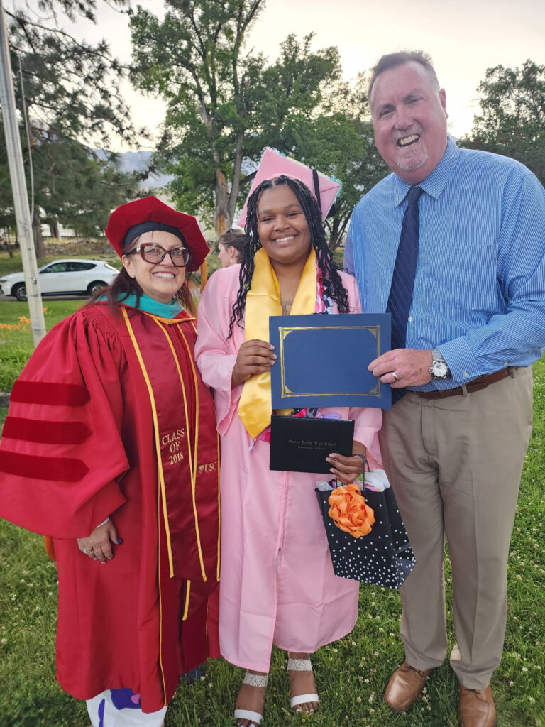 A smiling girl stands holding her scholarship award with two superintendents standing beside of her.