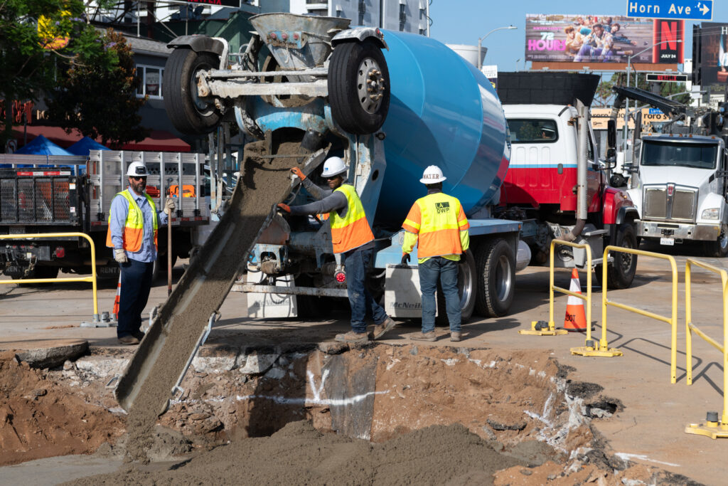 LADWP workers stand beside a slurry mix truck as the slurry is poured into an excavated area at a work site.